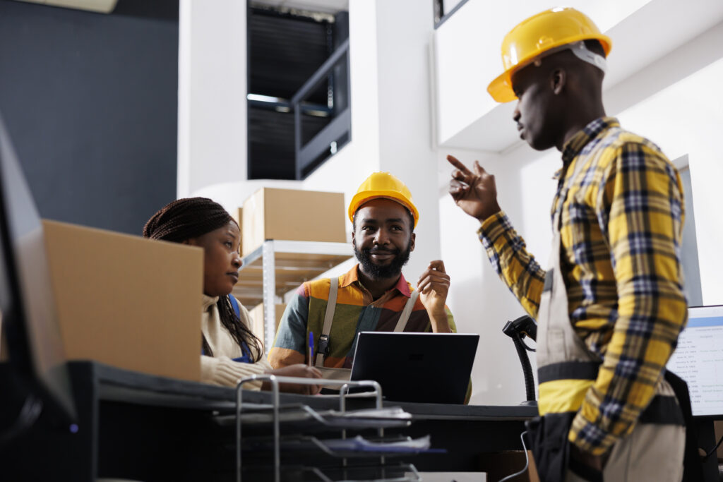 African american logistics managers team dicussing goods distribution at warehouse reception. Post office men and woman workers planning stock supply while chatting at counter desk
